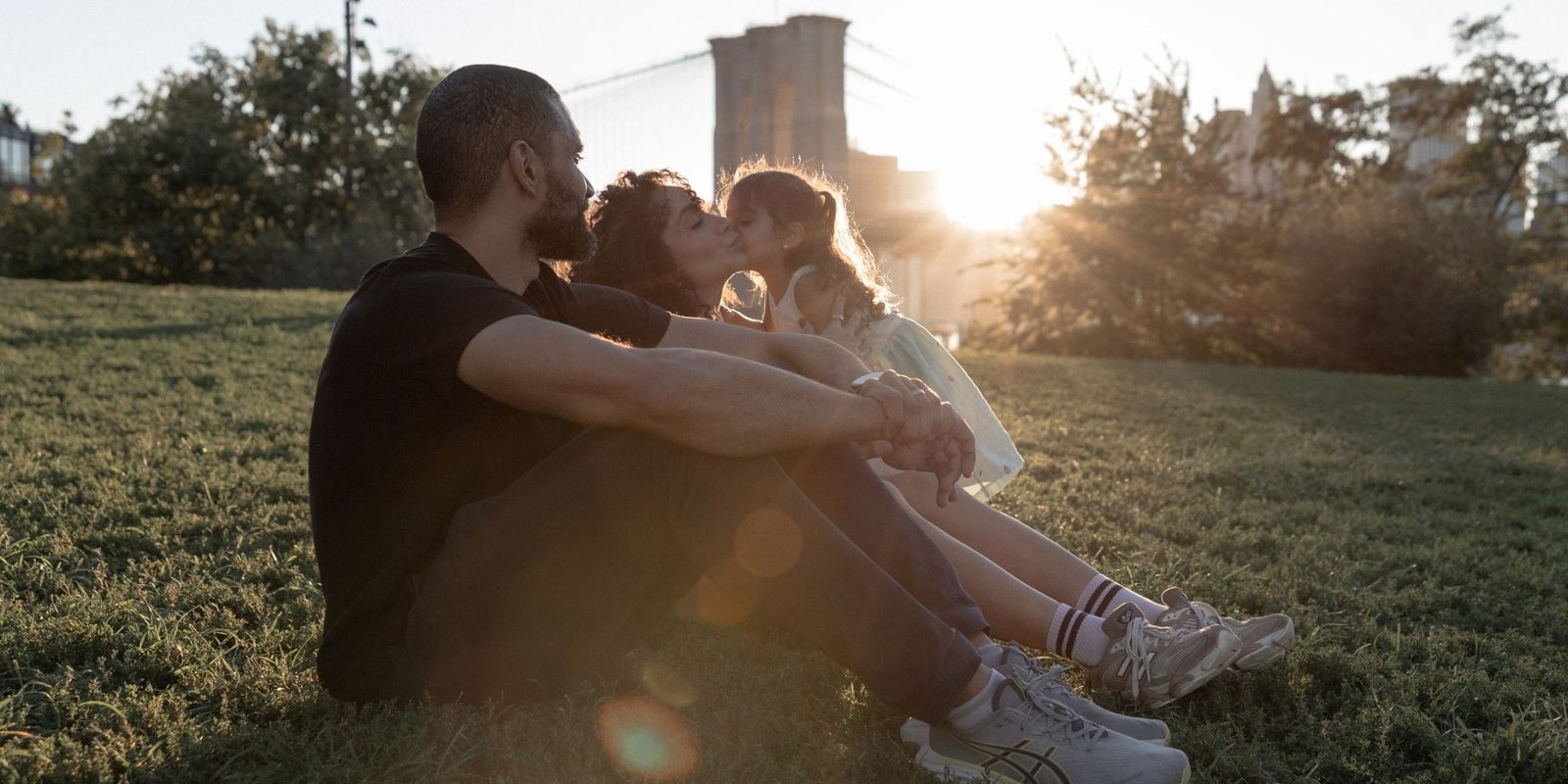 Kathy, o marido e a filha sentados na grama ao pôr do sol