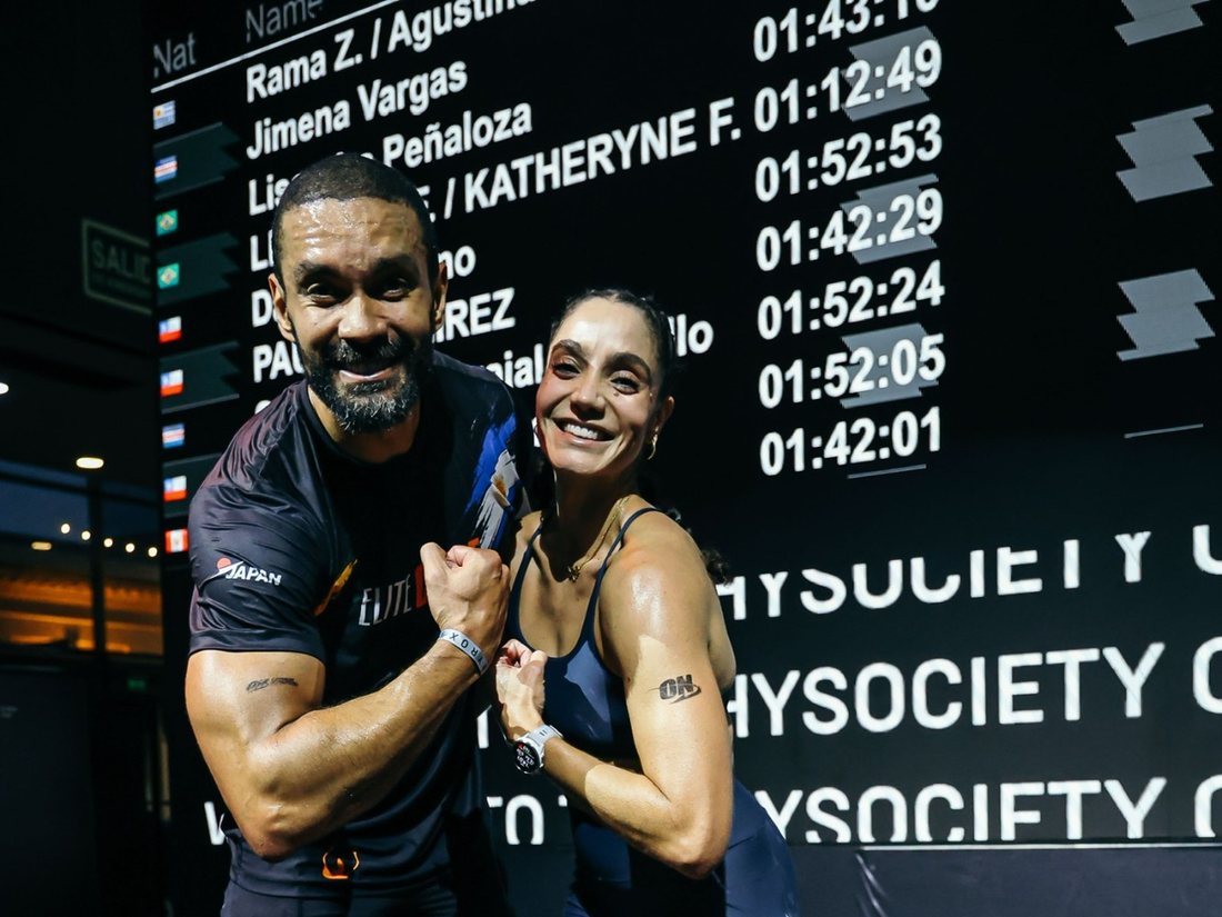 Kathy e o marido diante do placar do HYROX Buenos Aires com o tempo 01:12:49